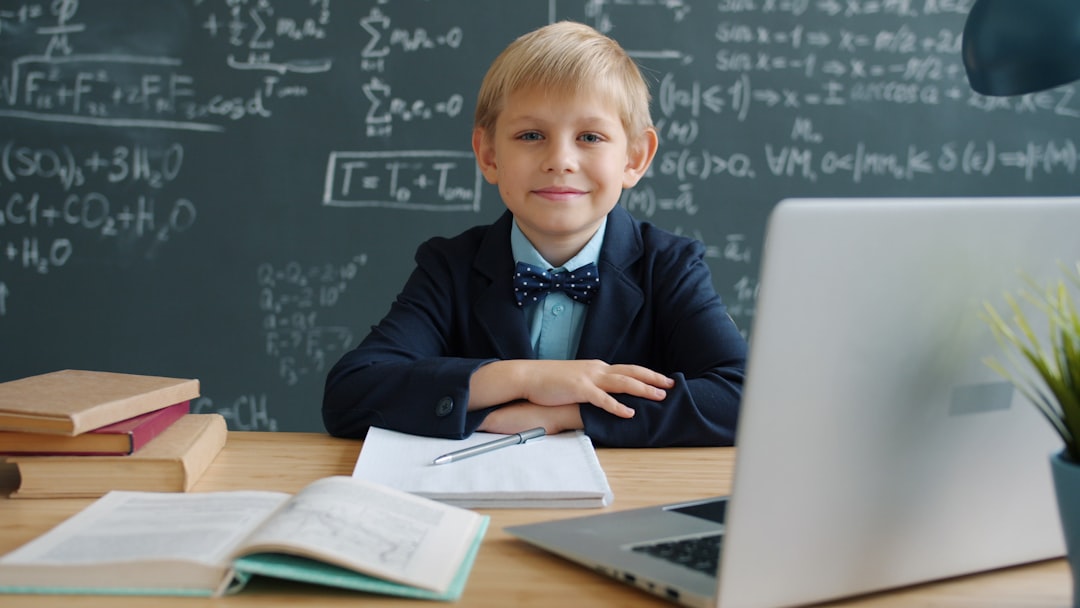 portrait of happy child wunderkind wearing suit sitting at desk in class with chalkboard full of formulas behind him. Educati