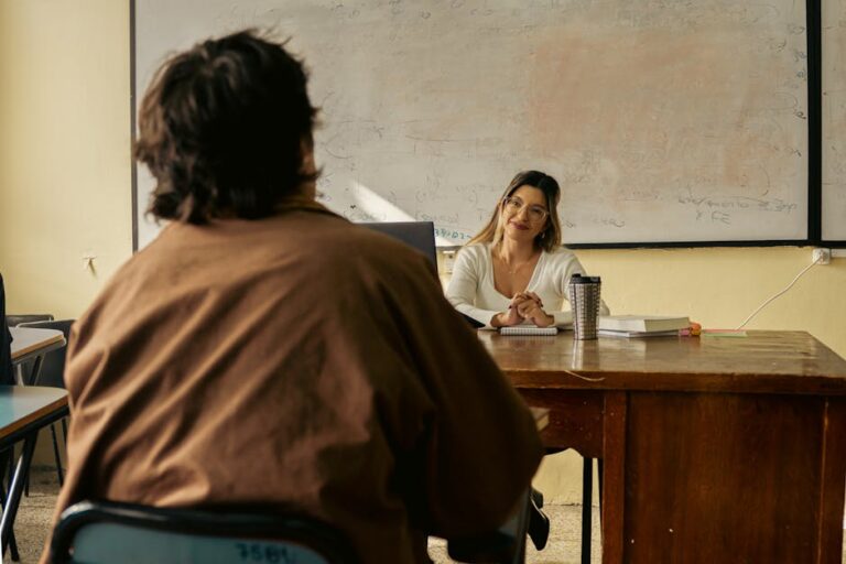 A teacher engages with a student in a university classroom setting, fostering learning.