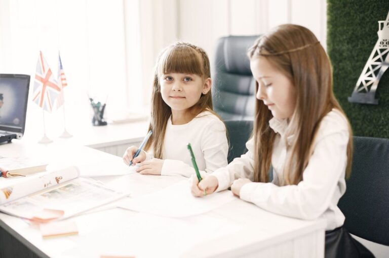 Two young girls writing at a desk in a bright office, symbolizing education and learning.