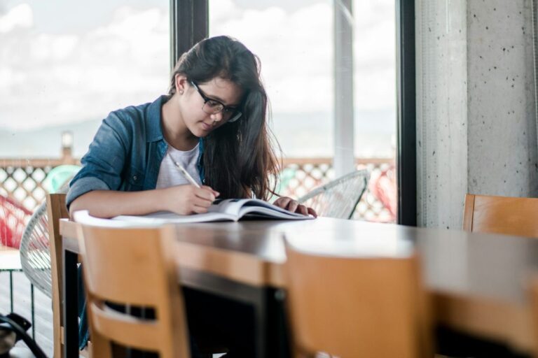 ESL student writing in a notebook by a window