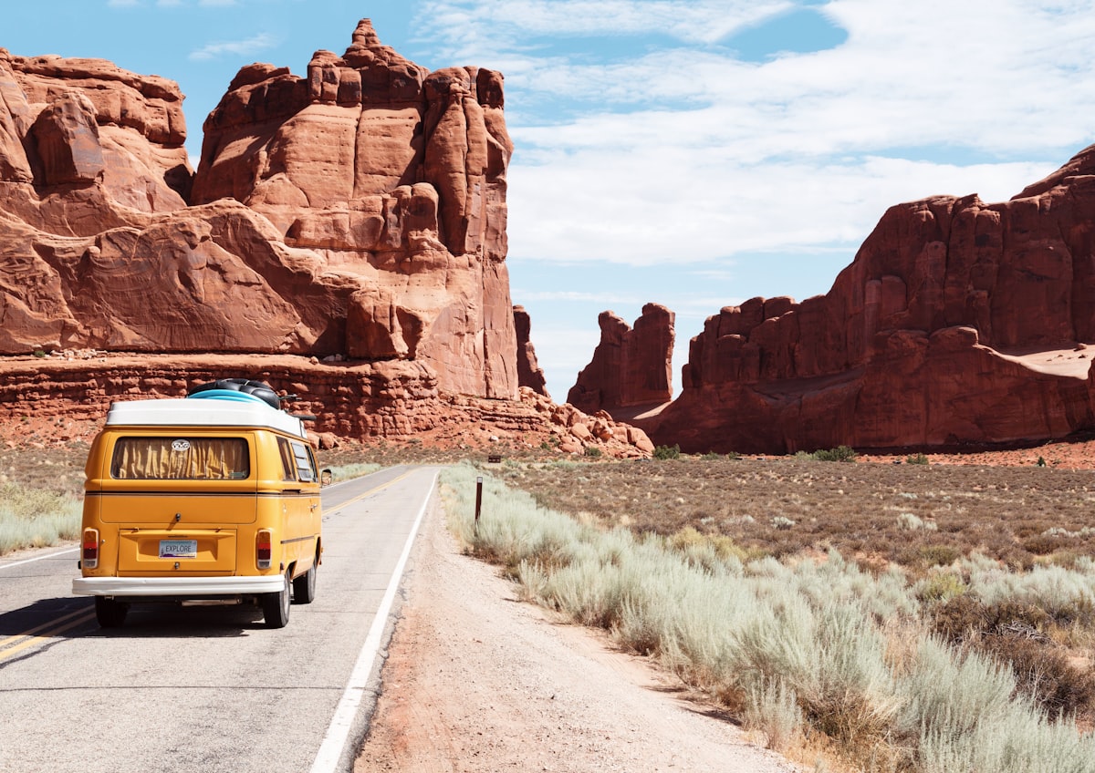 Yellow camper van driving down an open desert road past red rock formations, ready to hit the road Yellow camper van driving down an open desert road past red rock formations, ready to hit the road