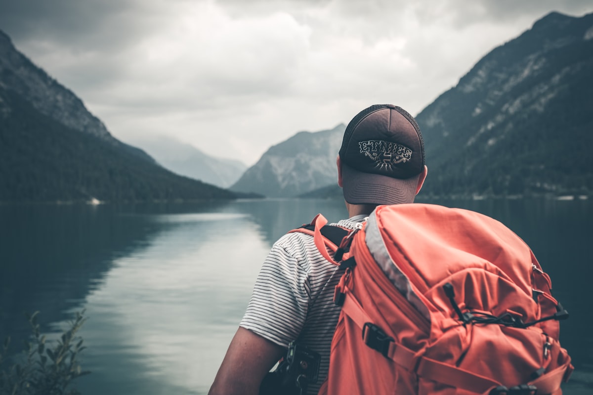 Backpacker with an orange rucksack gazing out over a misty mountain lake, itching to explore Backpacker with an orange rucksack gazing out over a misty mountain lake, itching to explore