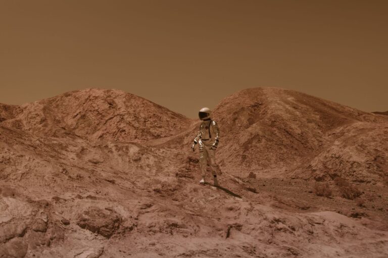 Astronaut in spacesuit explores barren, Mars-like desert terrain under brown sky.