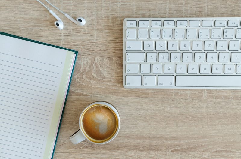 Notebook, keyboard and coffee on a desk set up for essay writing