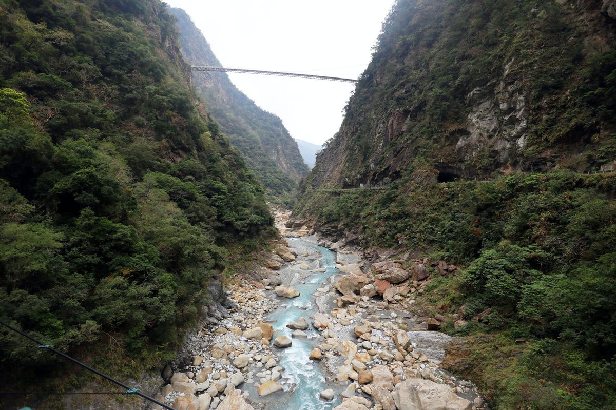 Panoramic view of a bridge over a river amidst lush green mountains in Taroko Gorge, Taiwan.