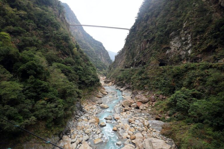 Panoramic view of a bridge over a river amidst lush green mountains in Taroko Gorge, Taiwan.