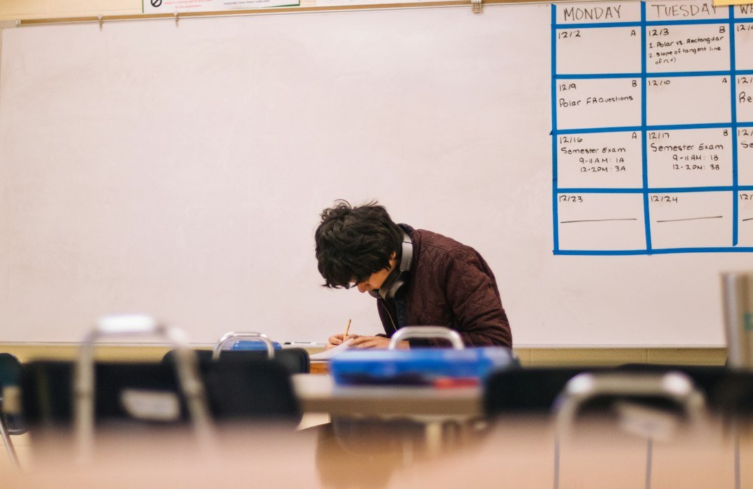 A student writing on paper at a desk in a classroom