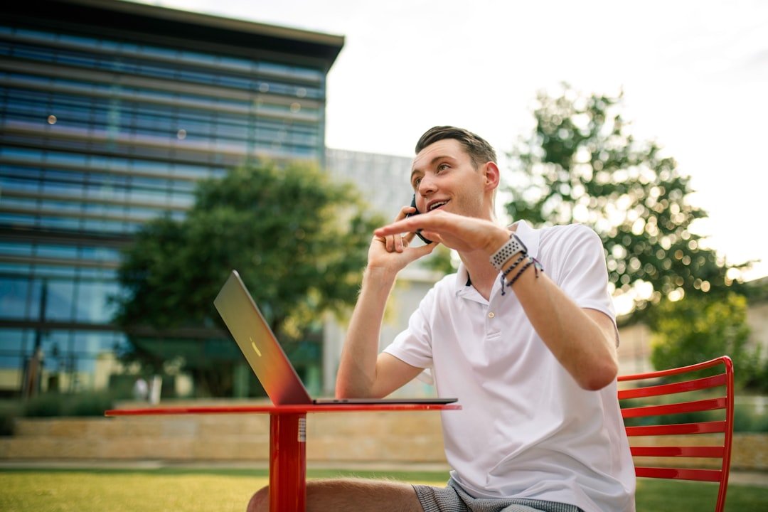 Male on phone outside working on his computer. 