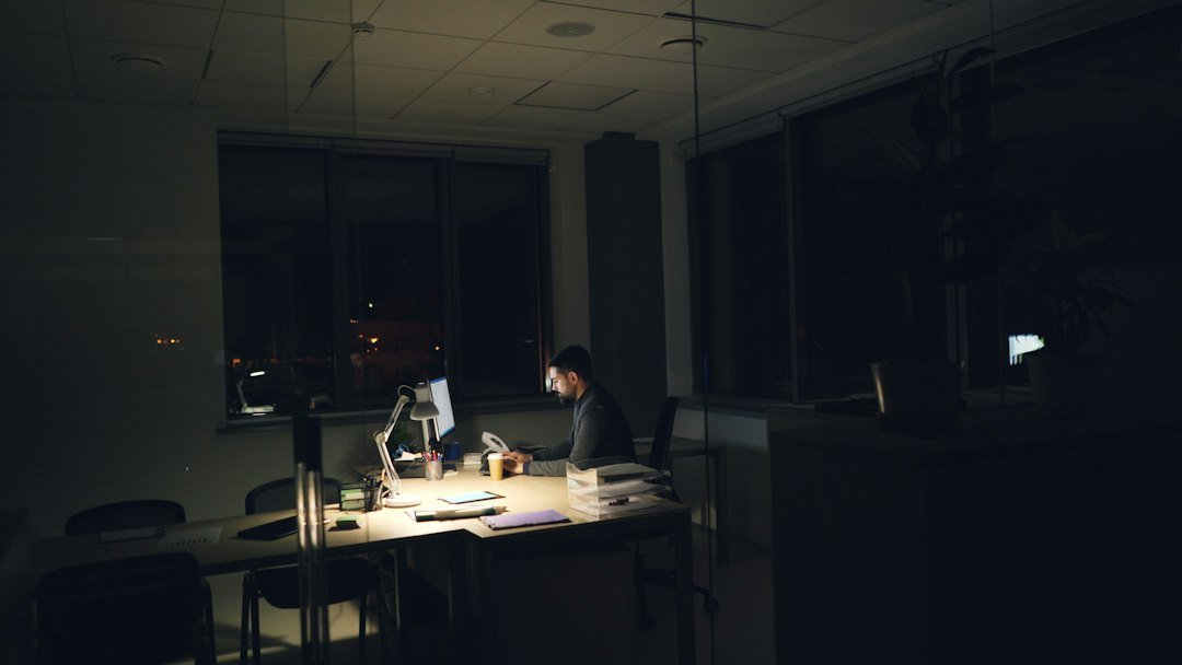 Tired businessman in suit and tie is using computer in office working at night sitting at worktable in dark room, looking at