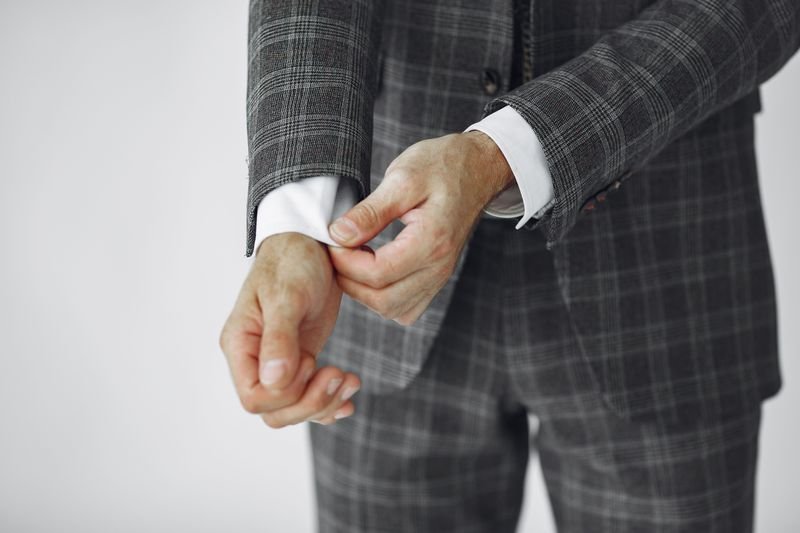Man adjusting a perfectly tailored plaid suit illustrating the idiom fit like a glove