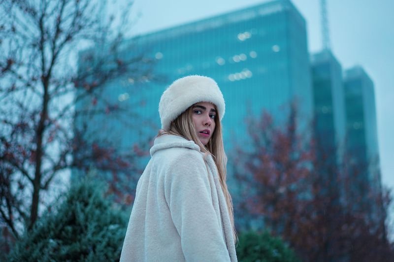 Stylish woman in a fur hat and coat on a city street illustrating keep it under your hat idiom