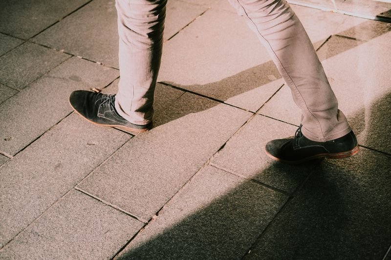 Close-up of legs in black shoes walking on stone pavement illustrating walk a mile in someones shoes idiom