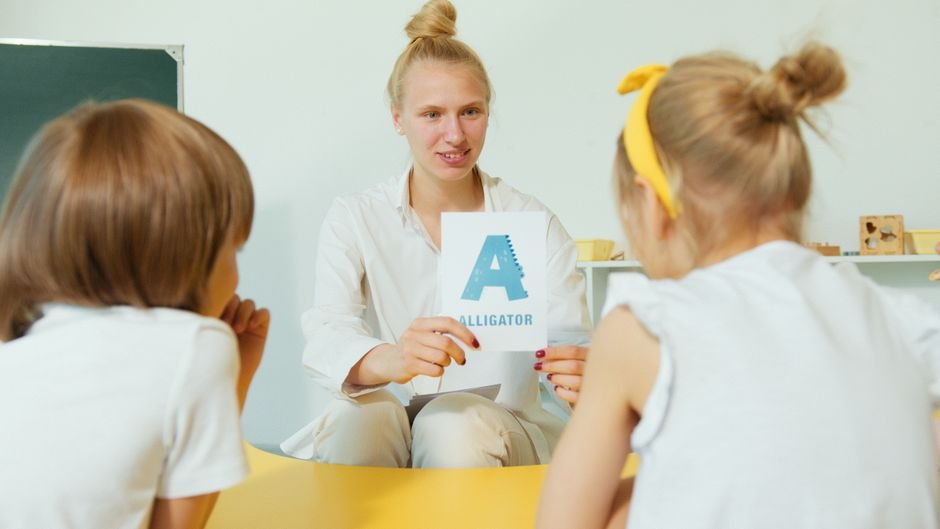 Teacher showing an alphabet flashcard to young students in a classroom