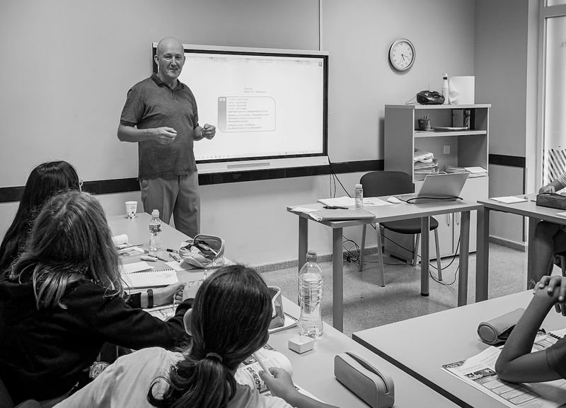 Teacher leading an English-only Direct Method lesson using a classroom whiteboard
