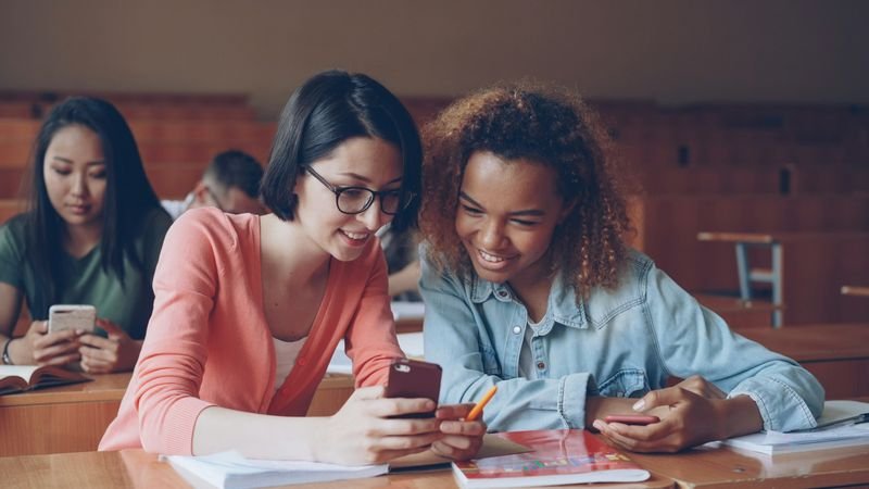 Two ESL students laughing while answering a Kahoot quiz question together on a phone