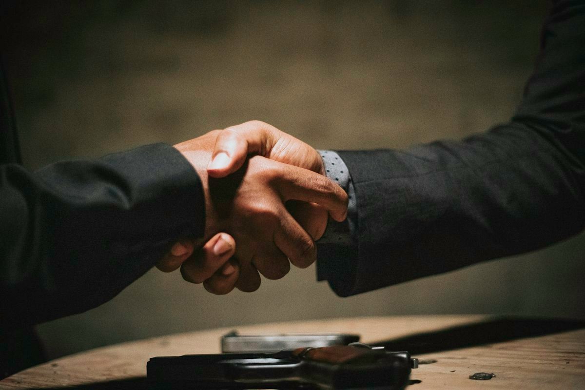 Two people shaking hands over a table, illustrating the idiom bury the hatchet
