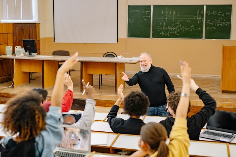 Teacher posing a driving question to engaged ESL students with hands raised