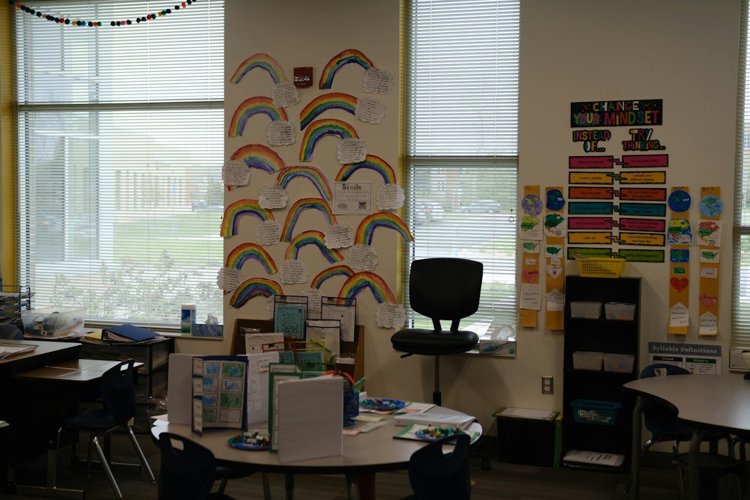 A classroom wall decorated with paper rainbows and educational posters near a round table