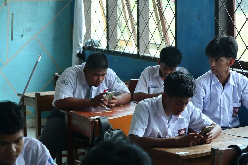 ESL students in uniform playing Quizlet Live on their phones in class