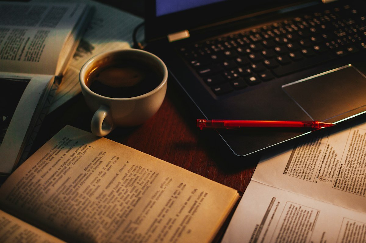 A cup of coffee between an open book and a laptop, illustrating cram for a test and a steep learning curve