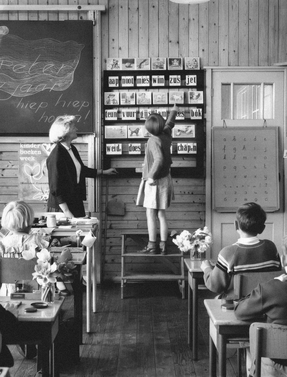 A black and white 1968 classroom scene with a teacher and student, illustrating old school and put your thinking cap on