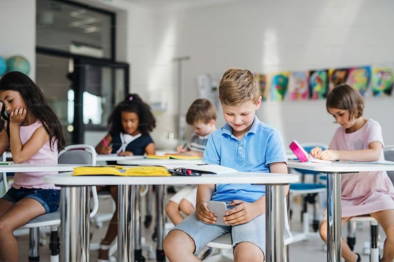 Young ESL student using a smartphone at his desk during class
